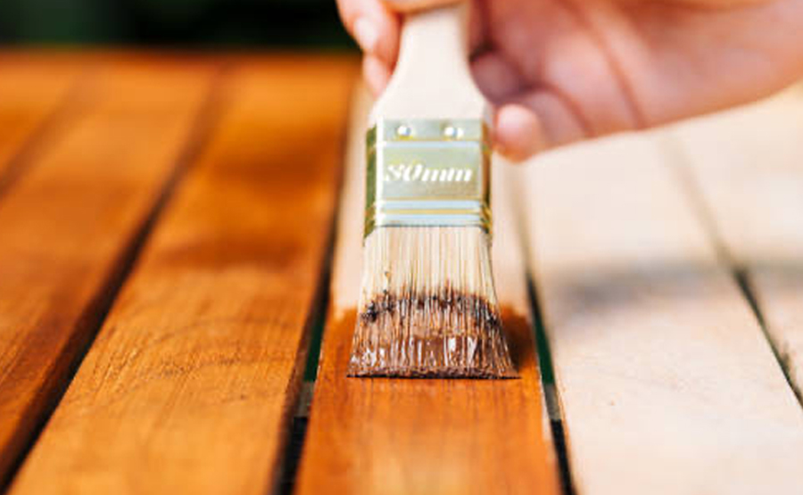 A person's hand staining a wooden table with a brush.