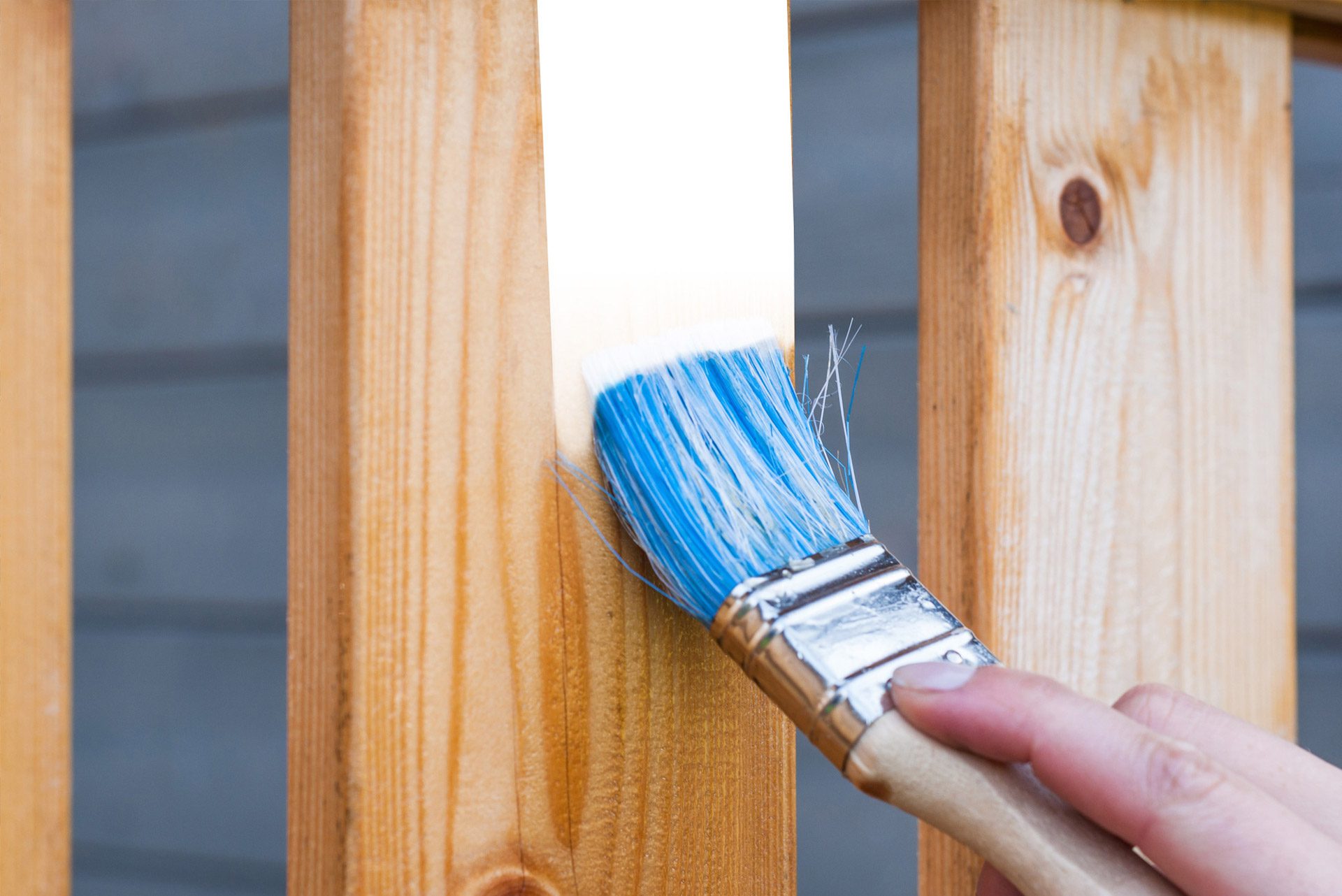 Man painting wood fence with paint brush.